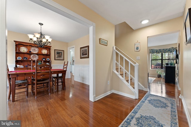 dining space with a wainscoted wall, stairway, wood finished floors, and a notable chandelier