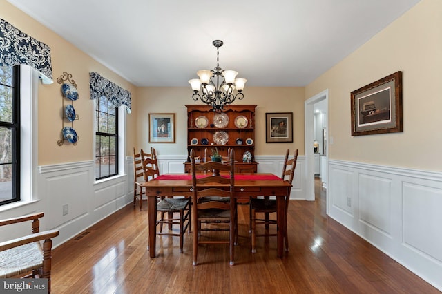 dining area featuring a decorative wall, a wainscoted wall, a notable chandelier, visible vents, and dark wood-style floors