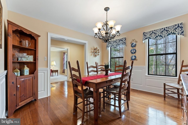 dining space featuring wood-type flooring, wainscoting, a notable chandelier, and a decorative wall