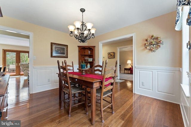 dining area featuring wainscoting, french doors, wood-type flooring, and an inviting chandelier