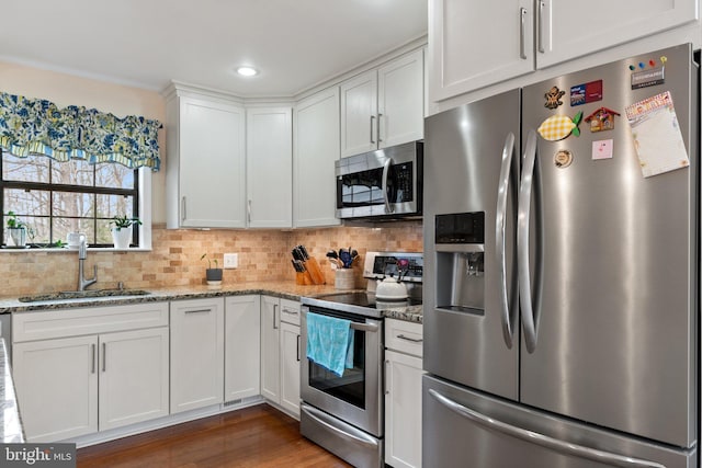 kitchen with tasteful backsplash, appliances with stainless steel finishes, white cabinetry, a sink, and light stone countertops