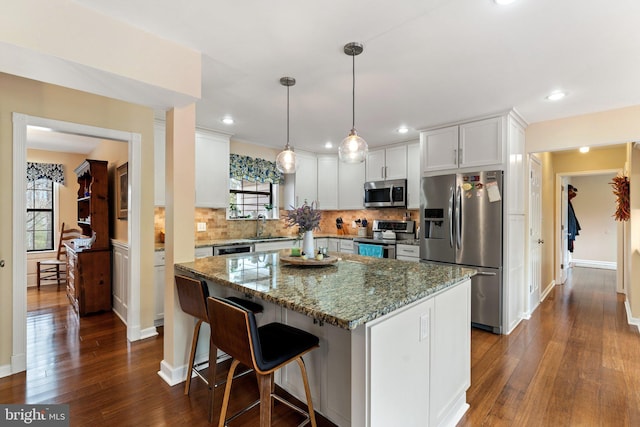 kitchen with a center island, appliances with stainless steel finishes, backsplash, light stone countertops, and dark wood-style floors