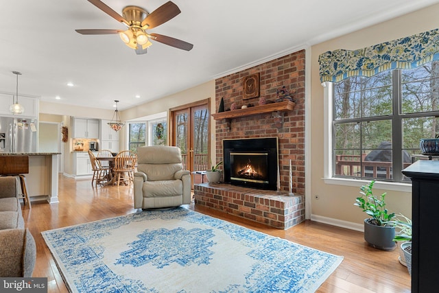 living area with light wood finished floors, recessed lighting, a ceiling fan, a brick fireplace, and baseboards