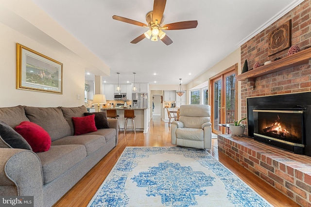 living room with a brick fireplace, light wood-style flooring, a ceiling fan, and recessed lighting