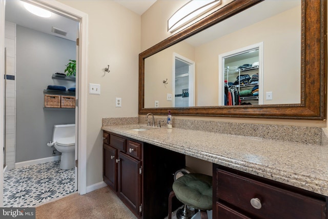 bathroom featuring toilet, vanity, visible vents, baseboards, and a walk in closet