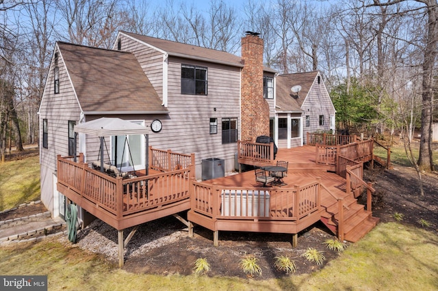 back of house with a deck, roof with shingles, a chimney, and central AC