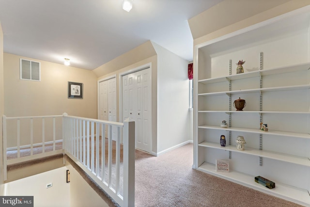 corridor featuring an upstairs landing, baseboards, visible vents, and carpet flooring