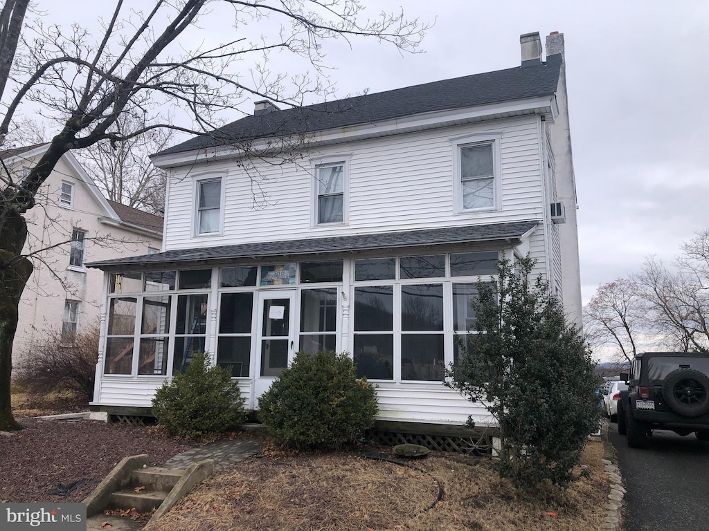 view of front of home featuring roof with shingles, a chimney, and a sunroom