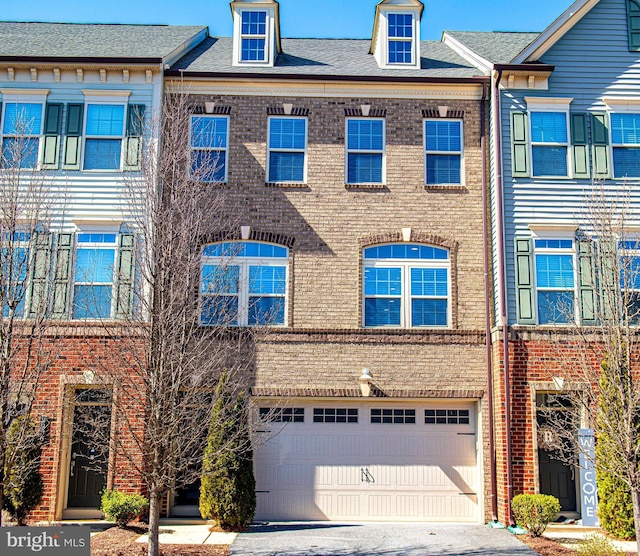 townhome / multi-family property with an attached garage, aphalt driveway, and brick siding