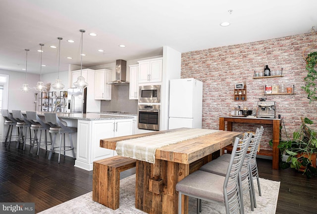 kitchen with dark wood-style flooring, a kitchen bar, appliances with stainless steel finishes, white cabinets, and wall chimney exhaust hood