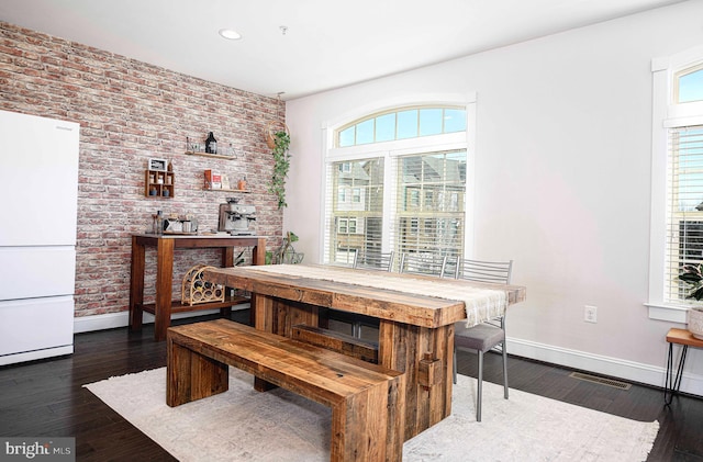 dining space with baseboards, brick wall, visible vents, and dark wood-type flooring