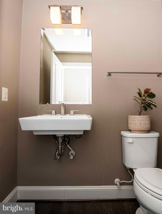 half bathroom with a sink, wood finished floors, toilet, and baseboards