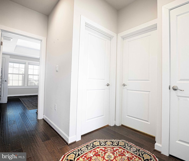 hall with visible vents, baseboards, and dark wood finished floors