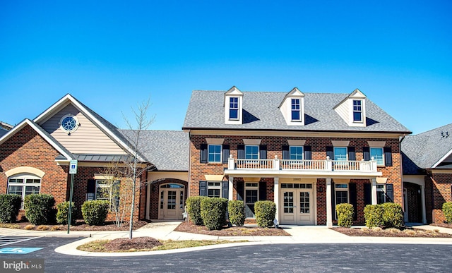 view of front of house featuring french doors, a shingled roof, a balcony, and brick siding