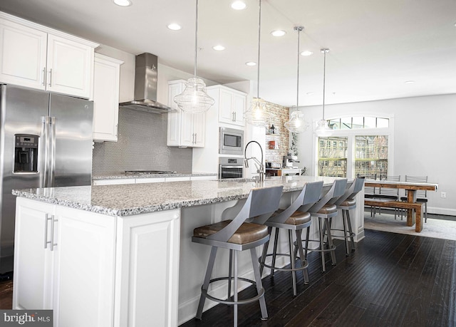 kitchen featuring dark wood-style flooring, stainless steel appliances, backsplash, white cabinets, and wall chimney exhaust hood