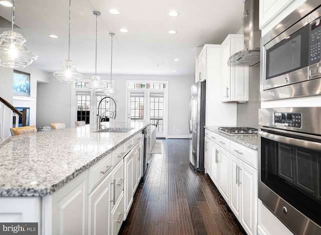 kitchen featuring dark wood-style flooring, appliances with stainless steel finishes, white cabinets, a sink, and wall chimney exhaust hood