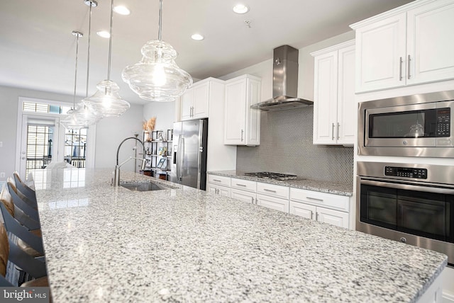 kitchen with stainless steel appliances, tasteful backsplash, white cabinets, a sink, and wall chimney exhaust hood