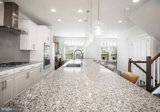 kitchen featuring stainless steel appliances, decorative backsplash, a sink, wall chimney range hood, and light stone countertops