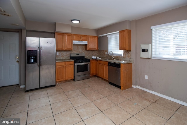 kitchen with under cabinet range hood, stainless steel appliances, decorative backsplash, and a sink