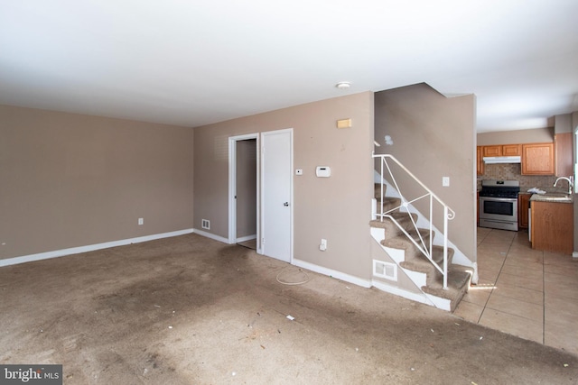 unfurnished living room with light tile patterned floors, baseboards, visible vents, a sink, and stairs