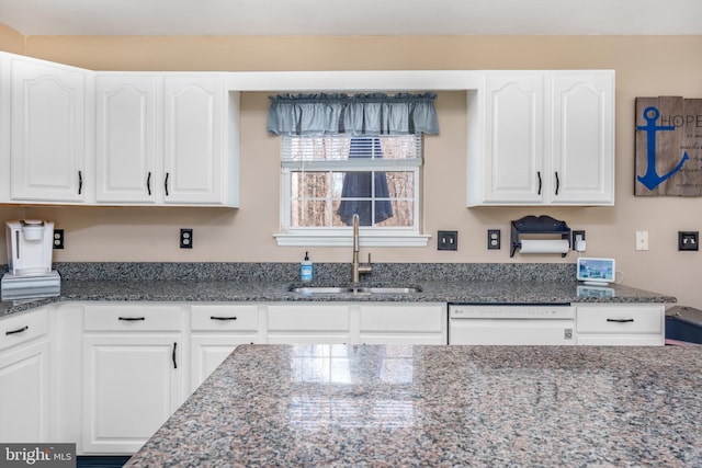 kitchen with dishwasher, dark stone countertops, a sink, and white cabinets