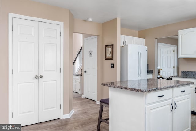 kitchen featuring light wood-style flooring, a kitchen island, white cabinets, freestanding refrigerator, and dark stone countertops