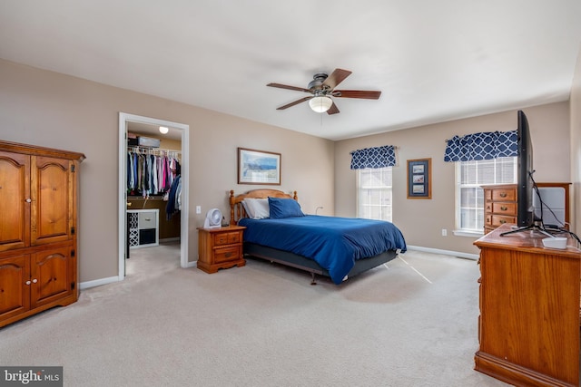 bedroom with a ceiling fan, light colored carpet, a spacious closet, and baseboards