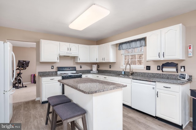 kitchen featuring under cabinet range hood, white appliances, a sink, white cabinetry, and a kitchen breakfast bar