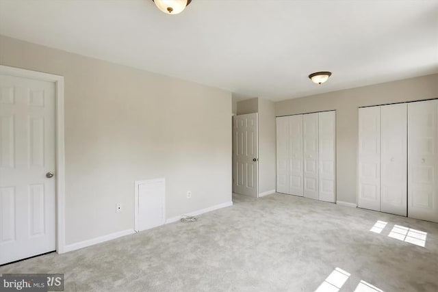 unfurnished bedroom featuring carpet flooring, baseboards, and two closets