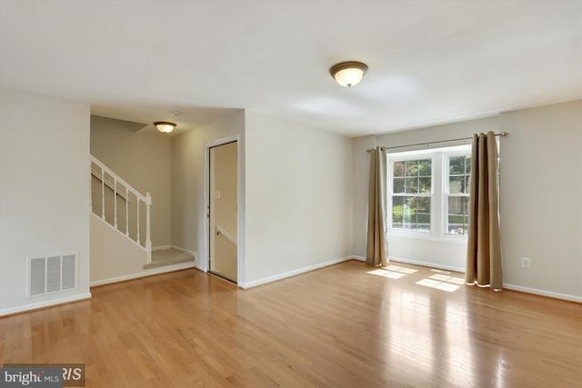 empty room with stairs, wood finished floors, visible vents, and baseboards