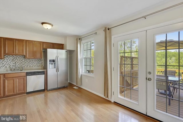 kitchen featuring french doors, brown cabinets, decorative backsplash, appliances with stainless steel finishes, and a sink