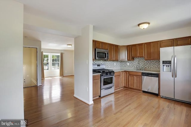 kitchen featuring light wood-style floors, appliances with stainless steel finishes, light countertops, and backsplash