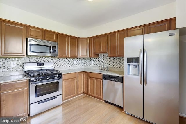 kitchen with appliances with stainless steel finishes, light wood-style floors, a sink, and backsplash