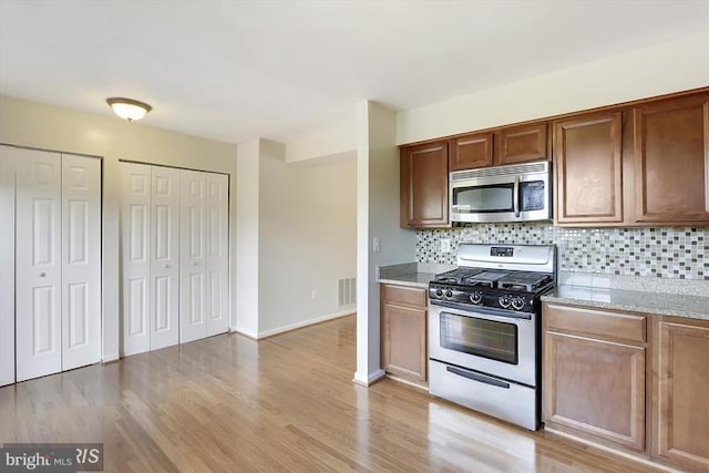 kitchen with appliances with stainless steel finishes, visible vents, light wood-style flooring, and tasteful backsplash