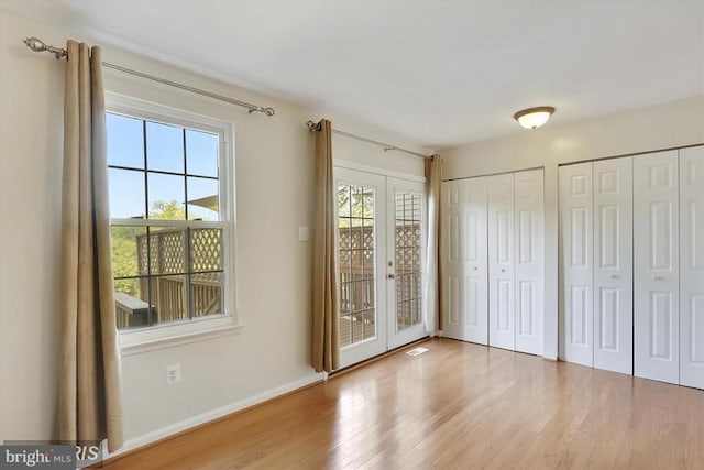 unfurnished bedroom featuring french doors, multiple windows, wood finished floors, and two closets