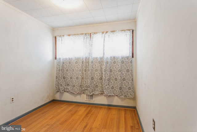 empty room with ornamental molding, visible vents, baseboards, and wood finished floors