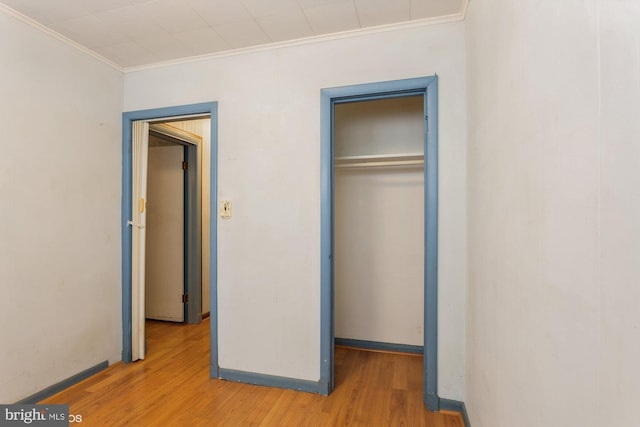 unfurnished bedroom featuring light wood-style floors, a closet, baseboards, and crown molding