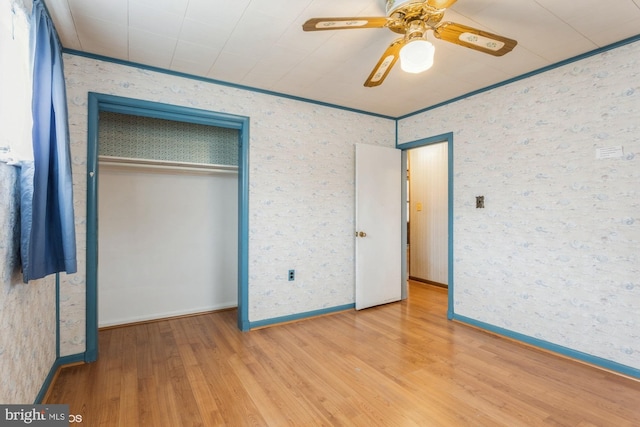 unfurnished bedroom with a closet, wood finished floors, crown molding, and wallpapered walls