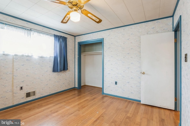 unfurnished bedroom with crown molding, a closet, visible vents, wood finished floors, and baseboards