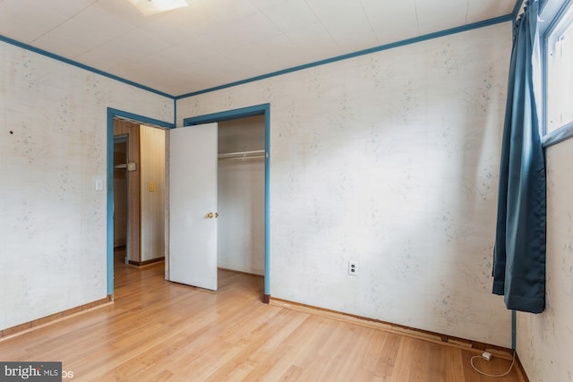 unfurnished bedroom with baseboards, a closet, ornamental molding, and wood finished floors