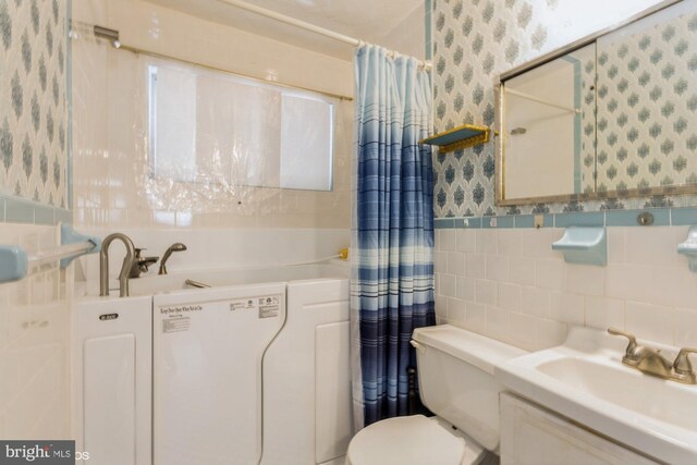 bathroom featuring tile walls, toilet, a sink, a shower with curtain, and wallpapered walls