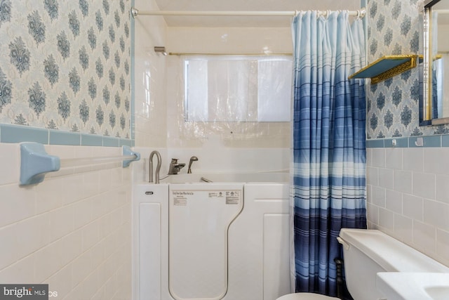 full bathroom featuring toilet, wallpapered walls, tile walls, and wainscoting