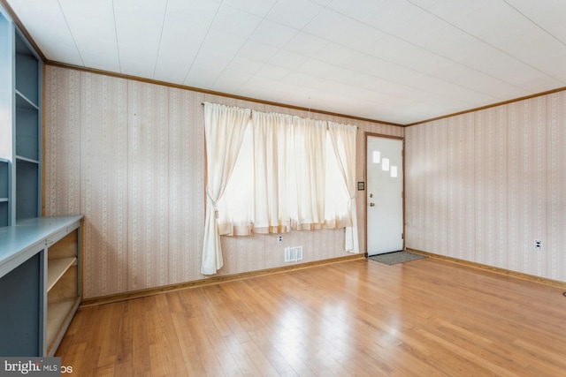 spare room featuring wallpapered walls, visible vents, wood finished floors, and ornamental molding