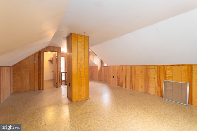 bonus room with vaulted ceiling and wood walls