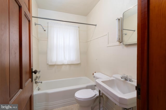 bathroom featuring washtub / shower combination, a sink, toilet, and tile walls