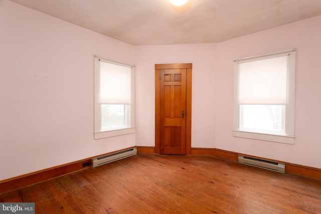 unfurnished room featuring a baseboard heating unit, wood-type flooring, and baseboards