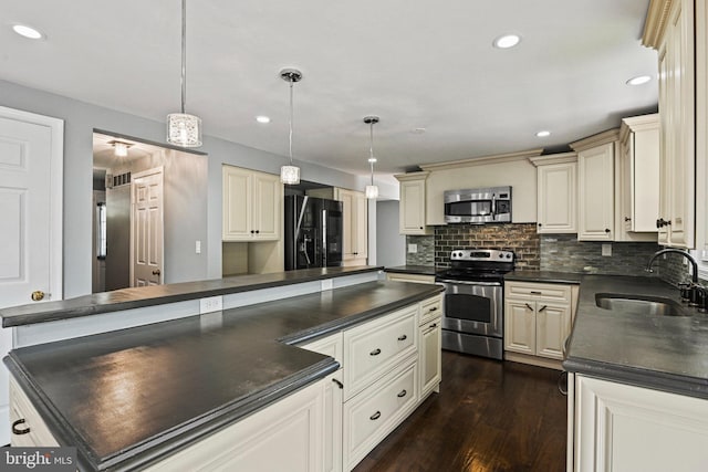 kitchen with dark countertops, dark wood-style flooring, stainless steel appliances, cream cabinetry, and a sink