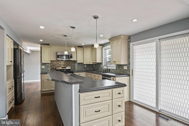 kitchen with cream cabinets, stainless steel appliances, a sink, visible vents, and dark countertops