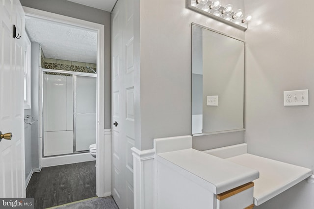 full bathroom featuring wood finished floors, a shower stall, toilet, and a textured ceiling