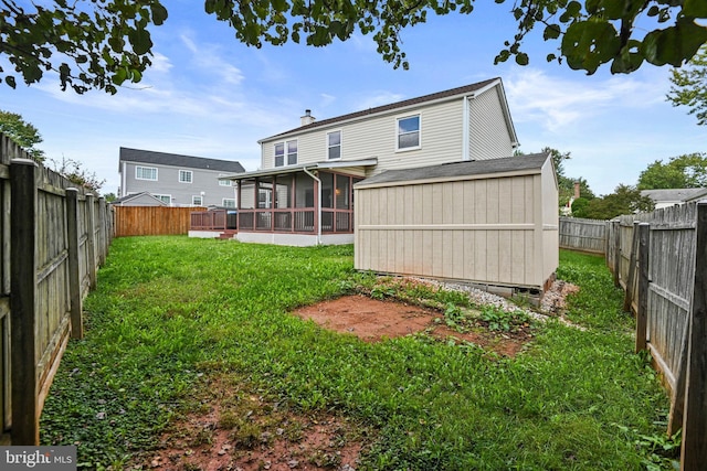 back of property featuring a lawn, a sunroom, a fenced backyard, a chimney, and an outbuilding